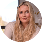 Lindsey Vonn, circular portrait, long blonde hair and a light pink top, smiling slightly at the camera in a bright indoor setting.
